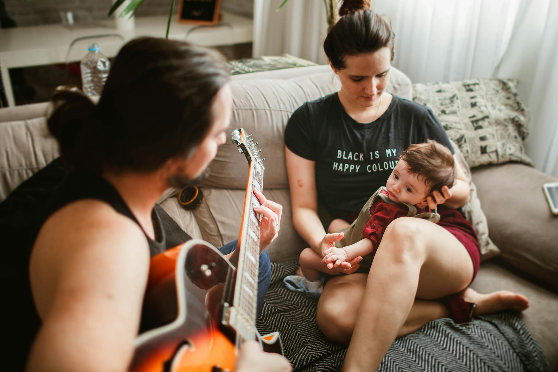 mother holds baby as father plays guitar and baby listens